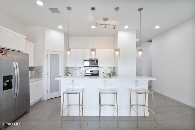 kitchen featuring pendant lighting, white cabinets, appliances with stainless steel finishes, a kitchen island, and tasteful backsplash