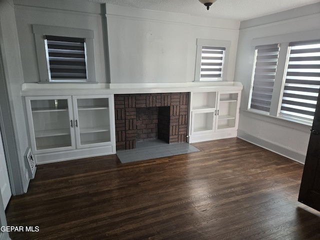 unfurnished living room with a brick fireplace, built in features, dark hardwood / wood-style floors, and a textured ceiling