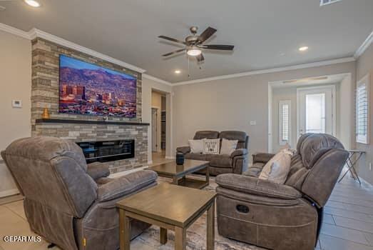 living room with ceiling fan, a stone fireplace, and ornamental molding