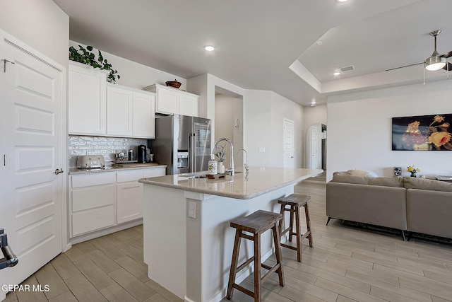 kitchen featuring high quality fridge, a kitchen bar, white cabinetry, ceiling fan, and a center island with sink