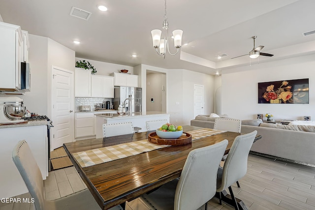 dining room with sink, ceiling fan with notable chandelier, and a tray ceiling