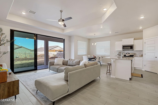 living room featuring ceiling fan with notable chandelier and a raised ceiling