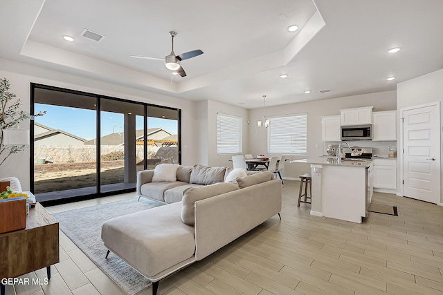 living room with ceiling fan with notable chandelier and a tray ceiling