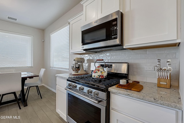 kitchen featuring decorative backsplash, white cabinetry, light stone countertops, appliances with stainless steel finishes, and plenty of natural light