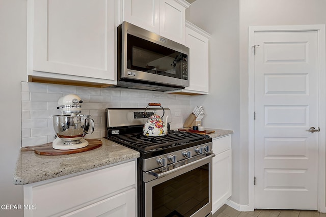 kitchen featuring light stone countertops, backsplash, appliances with stainless steel finishes, and white cabinetry