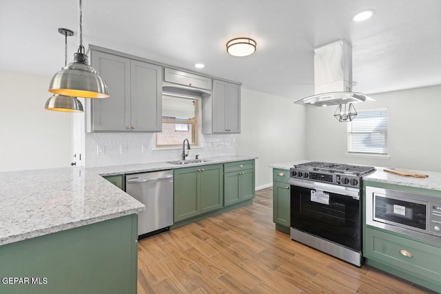 kitchen with sink, island exhaust hood, appliances with stainless steel finishes, green cabinetry, and light stone counters