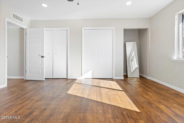 unfurnished bedroom with dark hardwood / wood-style flooring and two closets