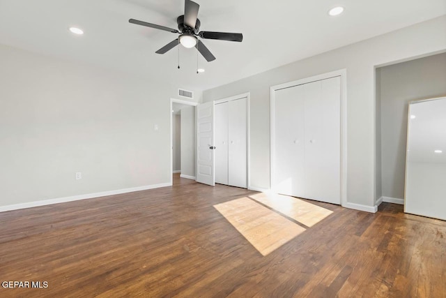 unfurnished bedroom with multiple closets, ceiling fan, and dark hardwood / wood-style flooring