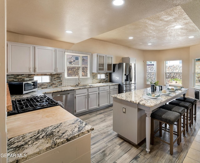 kitchen with a kitchen island, stainless steel appliances, a kitchen breakfast bar, sink, and light stone counters