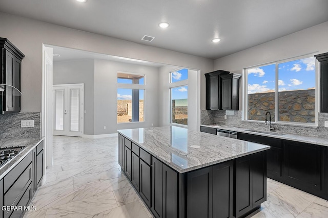 kitchen featuring a kitchen island, decorative backsplash, light stone counters, and sink