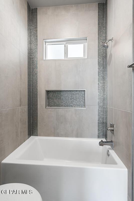 bathroom featuring toilet and tiled shower / bath