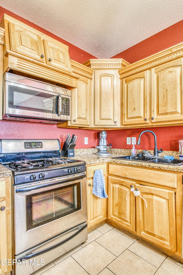 kitchen featuring a textured ceiling, light tile patterned floors, sink, stainless steel appliances, and light brown cabinets