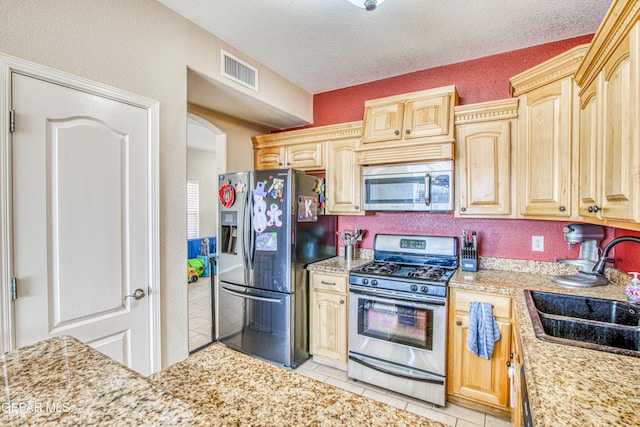 kitchen featuring a textured ceiling, stainless steel appliances, light brown cabinetry, sink, and light tile patterned floors