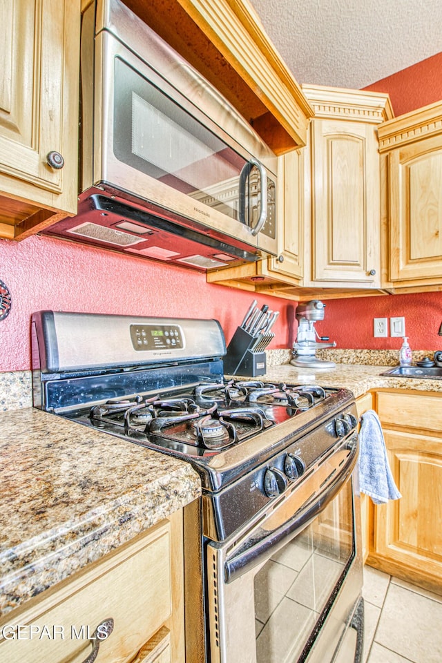 kitchen with a textured ceiling, appliances with stainless steel finishes, light brown cabinetry, sink, and light tile patterned floors