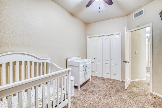 carpeted bedroom with ceiling fan, a nursery area, and a closet