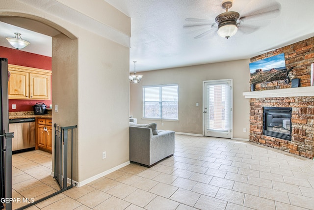 tiled living room with a brick fireplace, a textured ceiling, and ceiling fan with notable chandelier