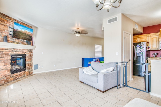 tiled living room featuring ceiling fan with notable chandelier and a stone fireplace