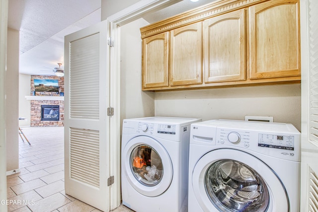 laundry room with ceiling fan, a brick fireplace, light tile patterned flooring, cabinets, and washer and clothes dryer