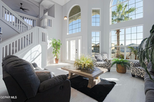 living room featuring ceiling fan, light hardwood / wood-style floors, a towering ceiling, and a healthy amount of sunlight