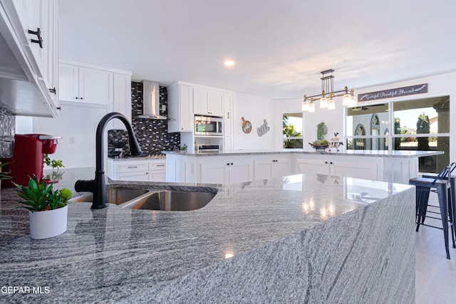 kitchen with decorative light fixtures, a center island, sink, light stone countertops, and white cabinets