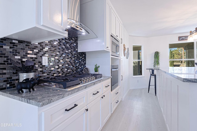 kitchen featuring white cabinets, appliances with stainless steel finishes, island exhaust hood, tasteful backsplash, and light stone counters