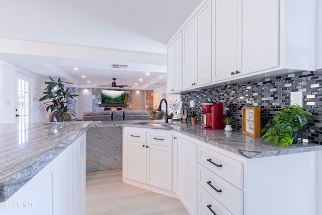 kitchen featuring a raised ceiling, decorative backsplash, sink, white cabinetry, and light stone countertops