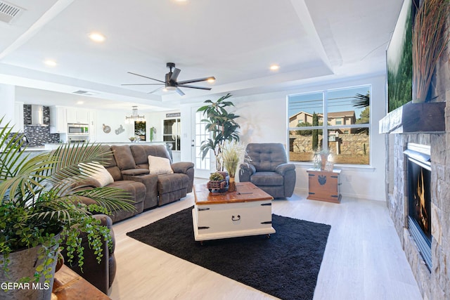 living room with ceiling fan, light wood-type flooring, and a tray ceiling