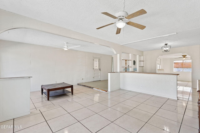 unfurnished living room featuring a textured ceiling, light tile patterned floors, and ceiling fan with notable chandelier