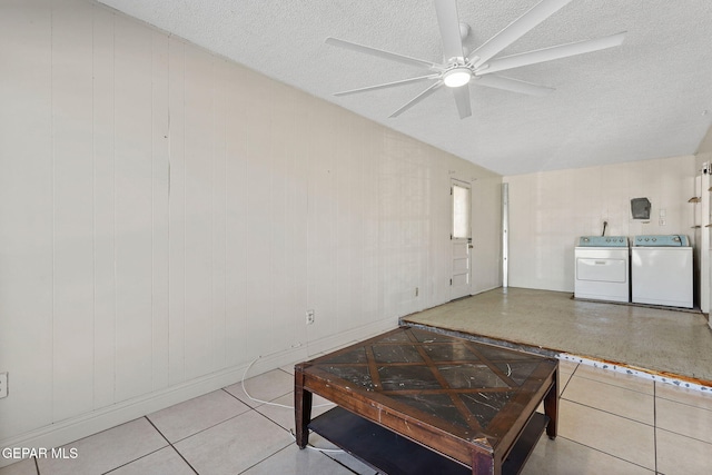 living room with light tile patterned floors, washing machine and clothes dryer, wooden walls, ceiling fan, and a textured ceiling