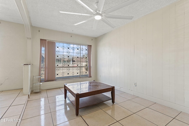 sitting room with a textured ceiling, ceiling fan, light tile patterned flooring, and wooden walls