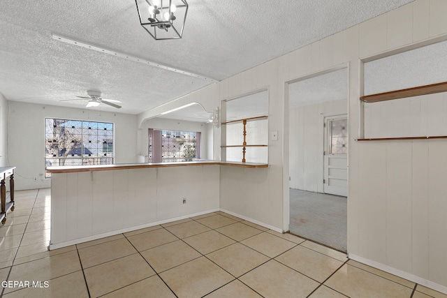 empty room featuring light tile patterned flooring, ceiling fan with notable chandelier, and a textured ceiling