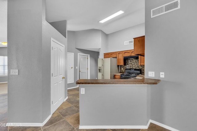 kitchen featuring tasteful backsplash, black range, kitchen peninsula, and stainless steel fridge