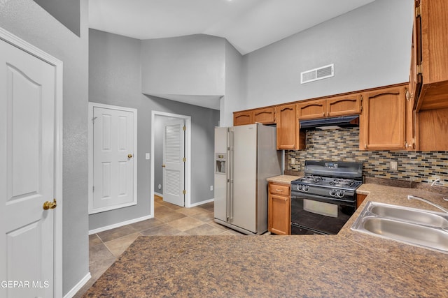 kitchen with decorative backsplash, gas stove, lofted ceiling, white refrigerator with ice dispenser, and sink