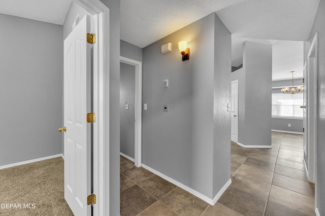 hall featuring dark carpet, a textured ceiling, and a notable chandelier