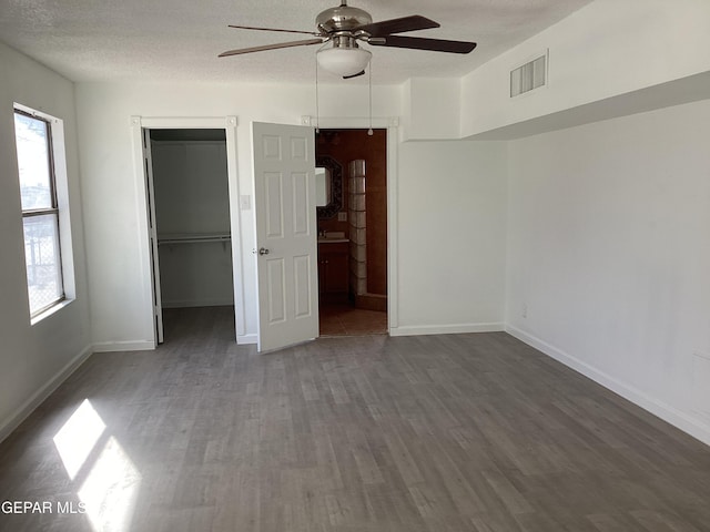 unfurnished bedroom with dark wood-type flooring, a closet, ceiling fan, and a walk in closet