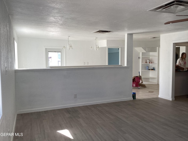 empty room with hardwood / wood-style flooring, a textured ceiling, built in features, and a notable chandelier