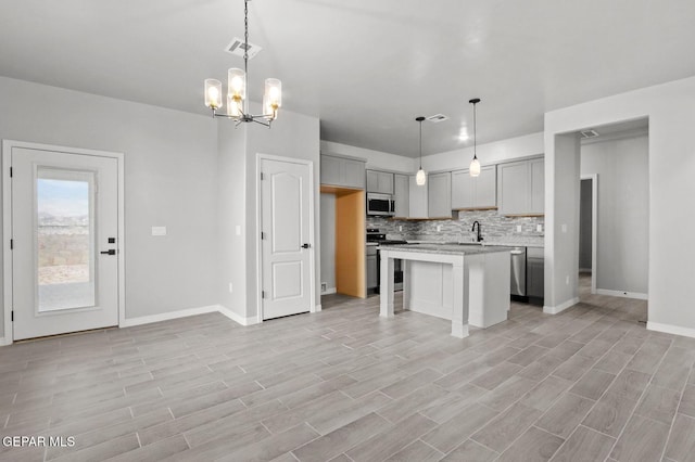 kitchen featuring gray cabinets, stainless steel appliances, a notable chandelier, decorative light fixtures, and a kitchen island