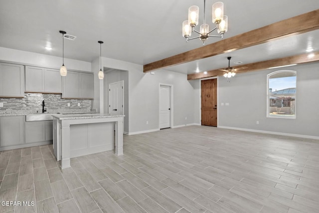 kitchen featuring gray cabinetry, hanging light fixtures, a kitchen island, ceiling fan with notable chandelier, and sink