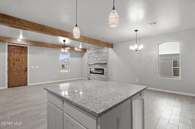 kitchen featuring a tiled fireplace, hanging light fixtures, ceiling fan with notable chandelier, light stone counters, and beamed ceiling