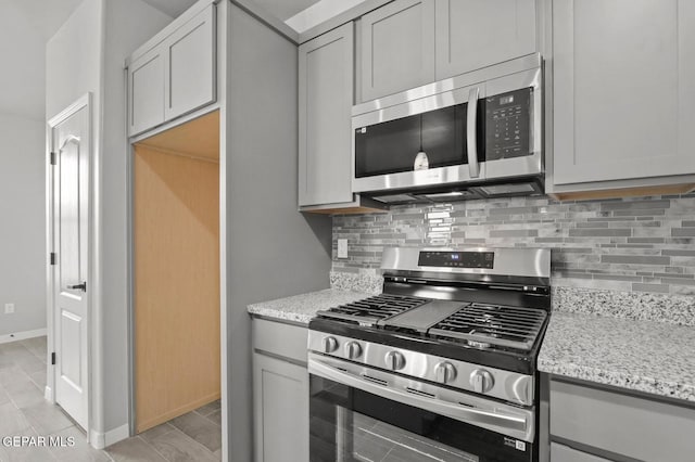 kitchen with stainless steel appliances, gray cabinetry, and light stone countertops