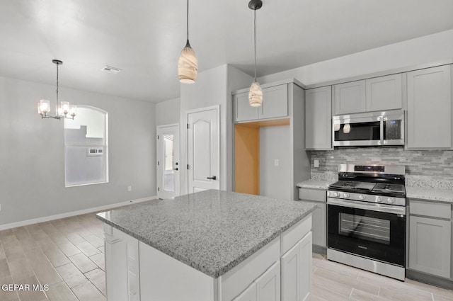 kitchen featuring gray cabinets, appliances with stainless steel finishes, backsplash, light stone counters, and a center island