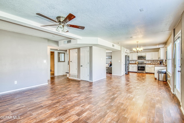 unfurnished living room featuring a textured ceiling, ceiling fan with notable chandelier, and sink