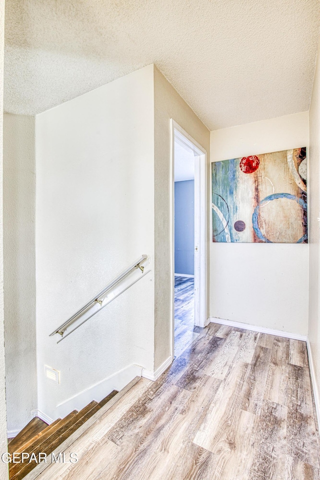 hall with a textured ceiling and light wood-type flooring