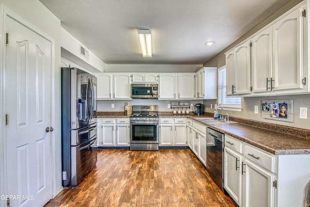 kitchen with sink, dark wood-type flooring, stainless steel appliances, a textured ceiling, and white cabinets