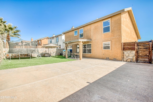 rear view of house featuring a patio area, a lawn, and a trampoline