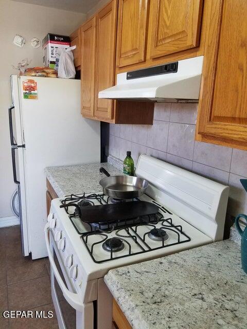 kitchen with light stone counters, decorative backsplash, dark tile patterned flooring, and white range with gas stovetop