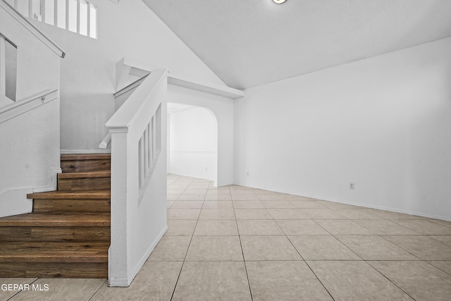 staircase with tile patterned floors and high vaulted ceiling