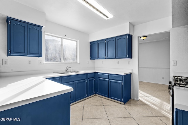 kitchen with light tile patterned floors, stainless steel gas stove, blue cabinetry, and sink