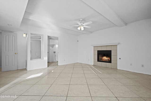 unfurnished living room featuring ceiling fan, a tiled fireplace, light tile patterned flooring, a textured ceiling, and beam ceiling