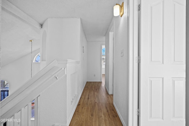 corridor with lofted ceiling, a textured ceiling, and hardwood / wood-style flooring